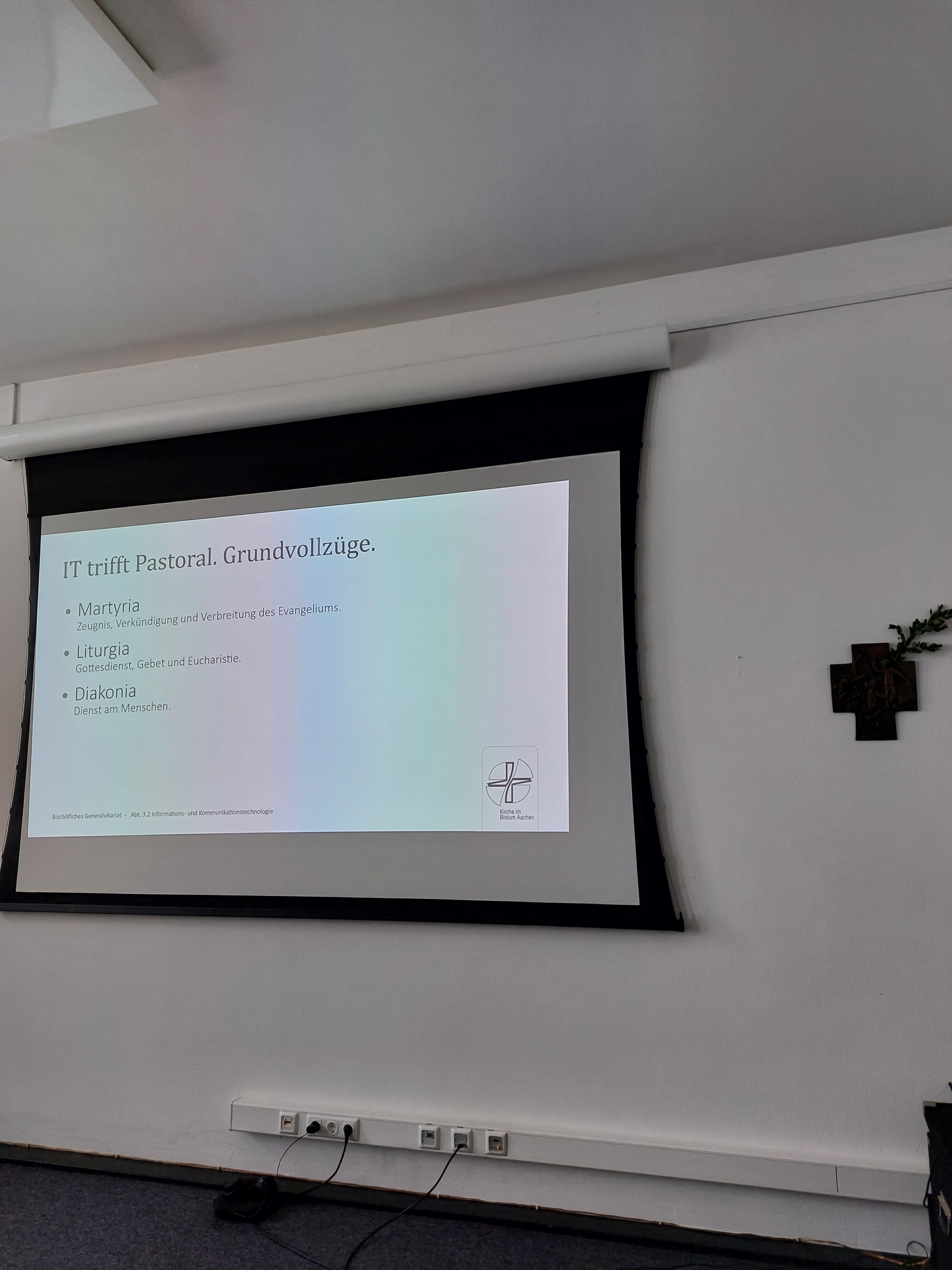 Präsentation im Tagungsraum. Die Folie trägt den Titel: IT trifft Pastoral. Grundvollzüge.