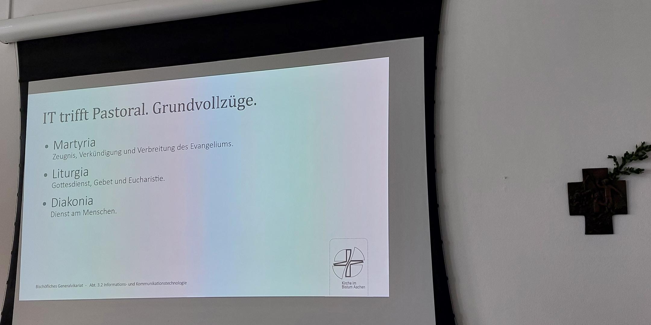 Präsentation im Tagungsraum. Die Folie trägt den Titel: IT trifft Pastoral. Grundvollzüge.