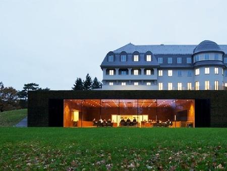 (c) Parlament der Deutschsprachigen Gemeinschaft Belgiens (Eupen) Außenansicht des Parlamentsgebäudes, ein ehemaliges Sanatorium aus dem Jahr 1915 mit einem vorgebauten Plenarsaal mit Glasfront.