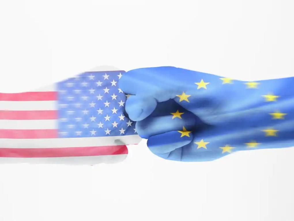 Zwei Hände geben sich einen Faustgruß, die linke Hand hat die Flagge der USA wie einen Handschuh angezogen, die rechte die Flagge der Europäischen Union.