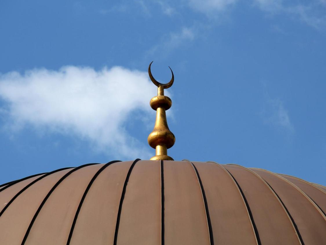Oberer Teil der Kuppel einer Mosche, darauf ein Halbmond vor dem Himmel.