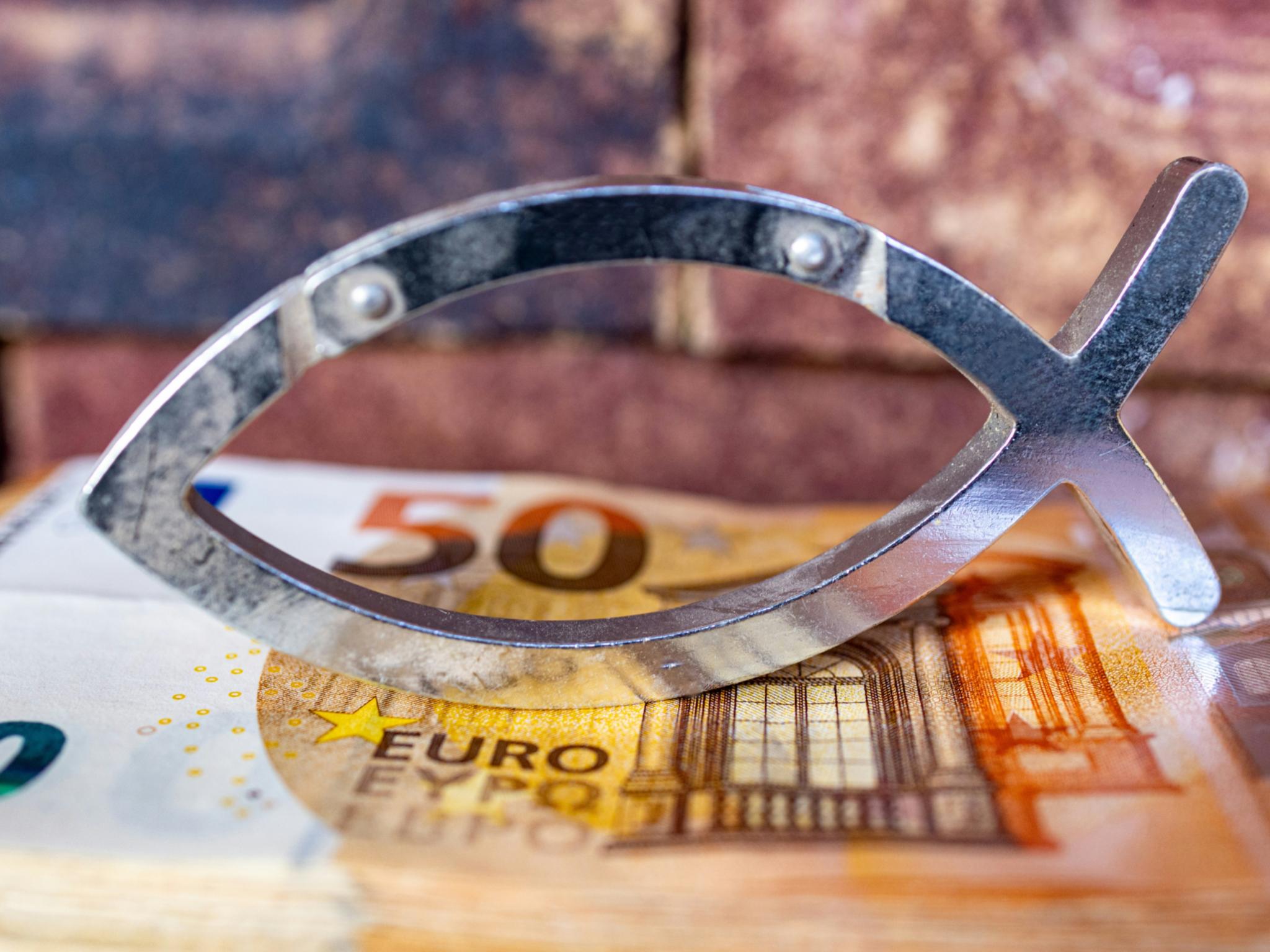 Das christliche Symbol eines Fisches ist aus Metall in zwei schlichten Linien gebildet. Es steht auf einem 50-Euro-Schein.