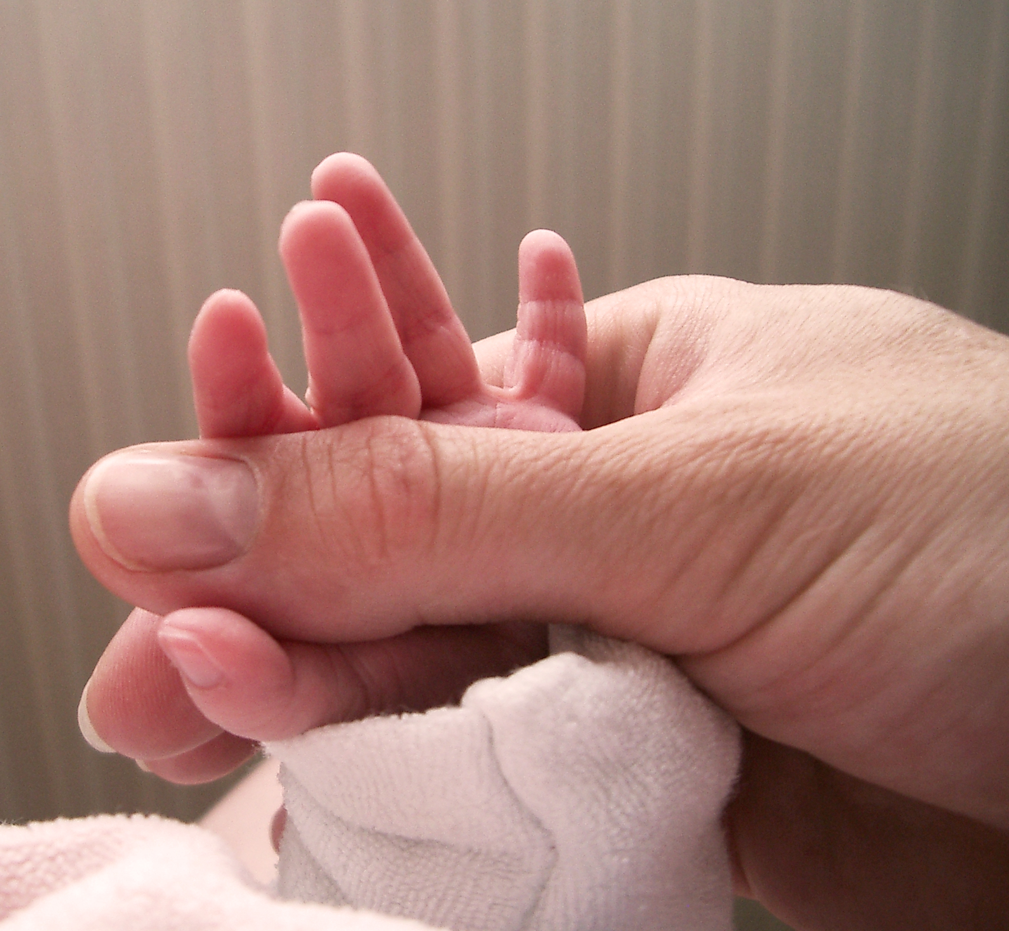 Die Hand einer Mutter umfasst die kleine Hand eines Babys.