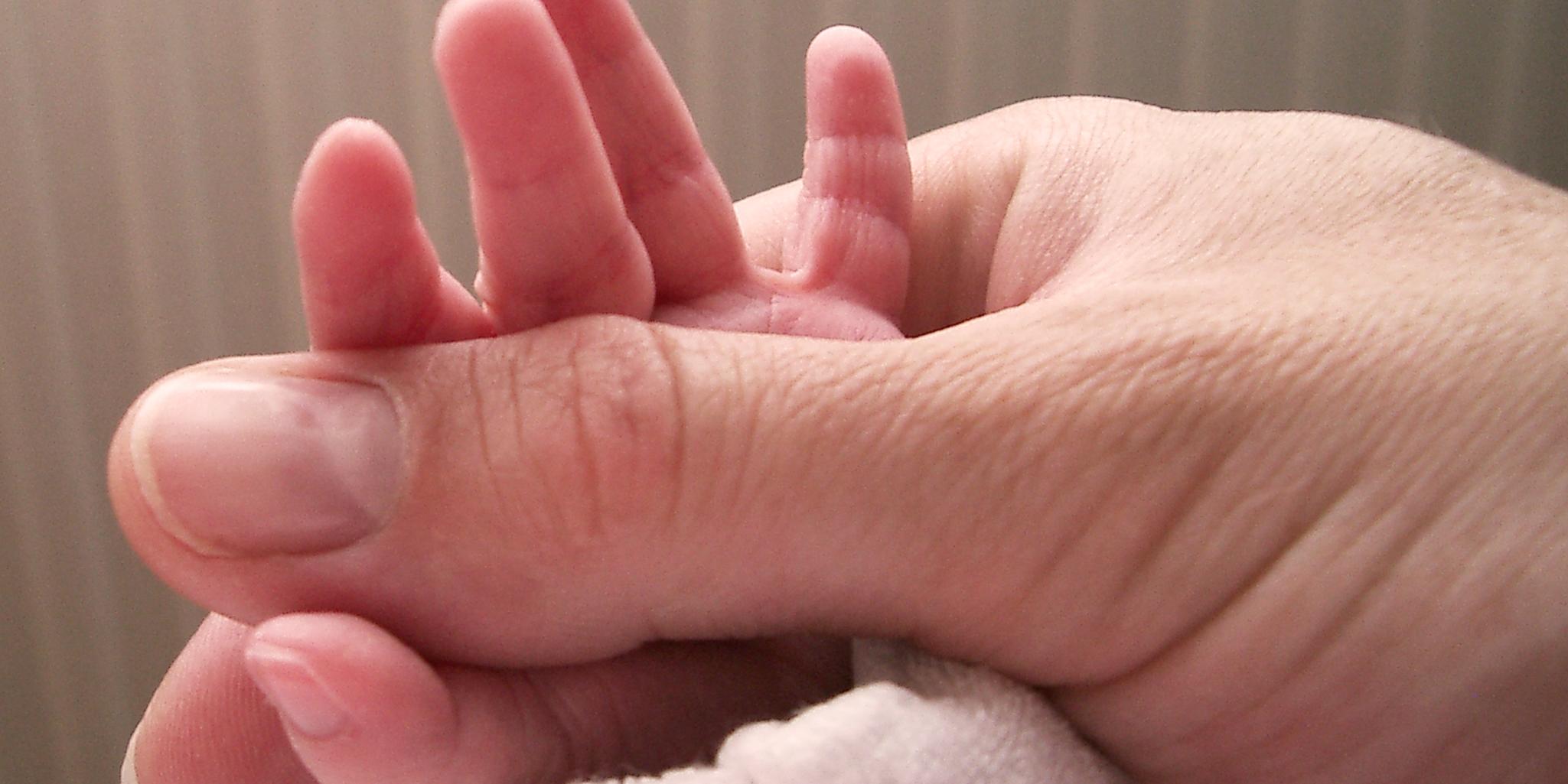 Die Hand einer Mutter umfasst die kleine Hand eines Babys.