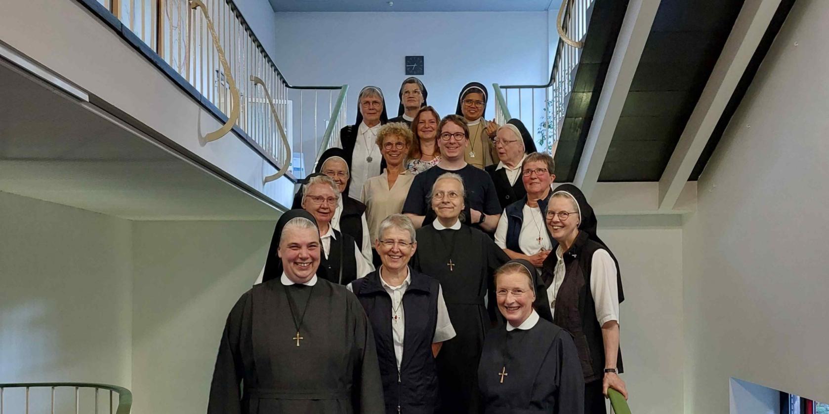 Schwestern in Ordenstracht und einige Mitarbeitende der Akademie stehen auf einer Treppe als Gruppenbild.