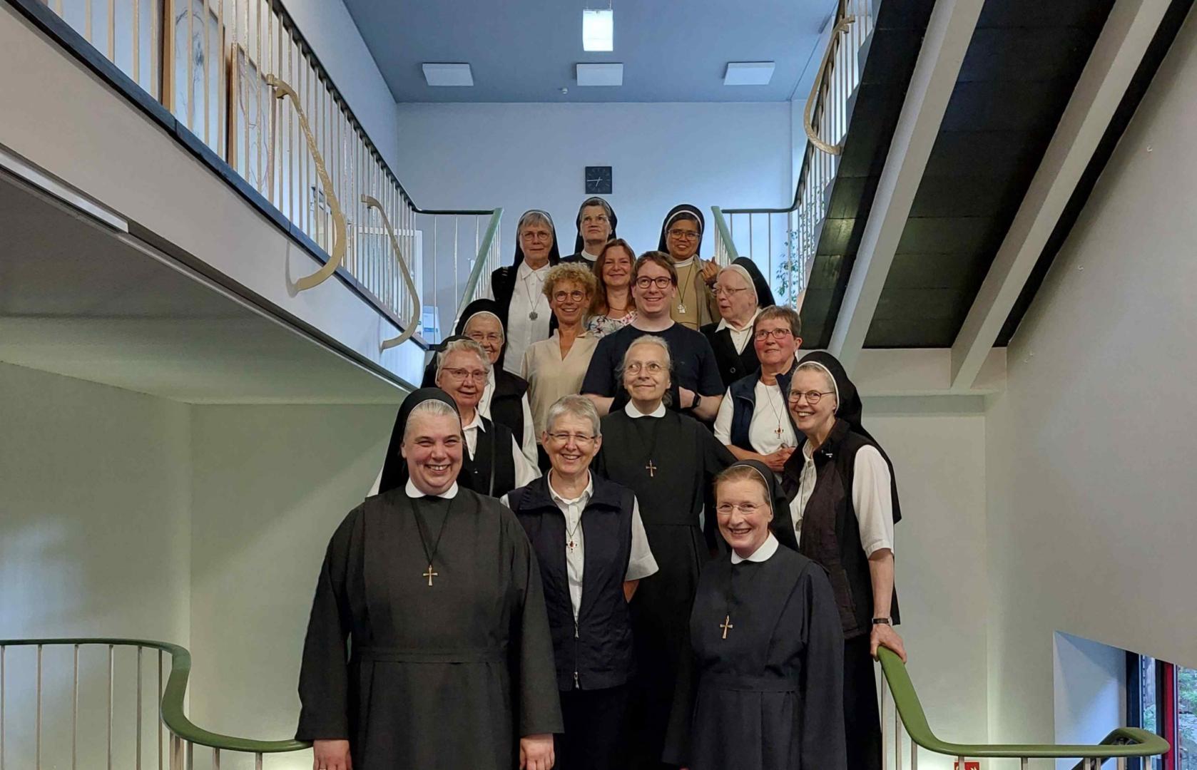Schwestern in Ordenstracht und einige Mitarbeitende der Akademie stehen auf einer Treppe als Gruppenbild.
