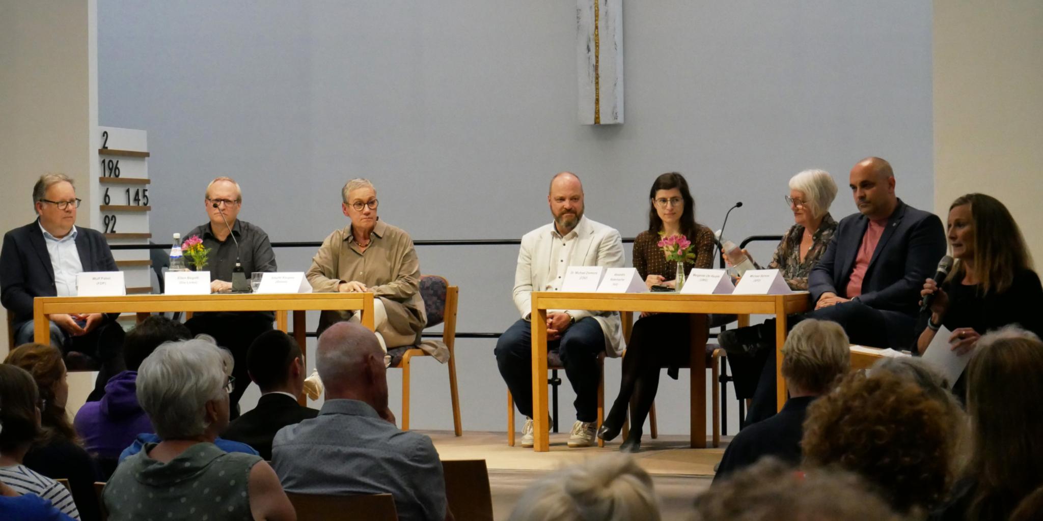 Personen, die bei der Kommunalwahl für das Amt des Oberbürgermeisters, der Oberbürgermeisterin kandidieren, an Tischen.