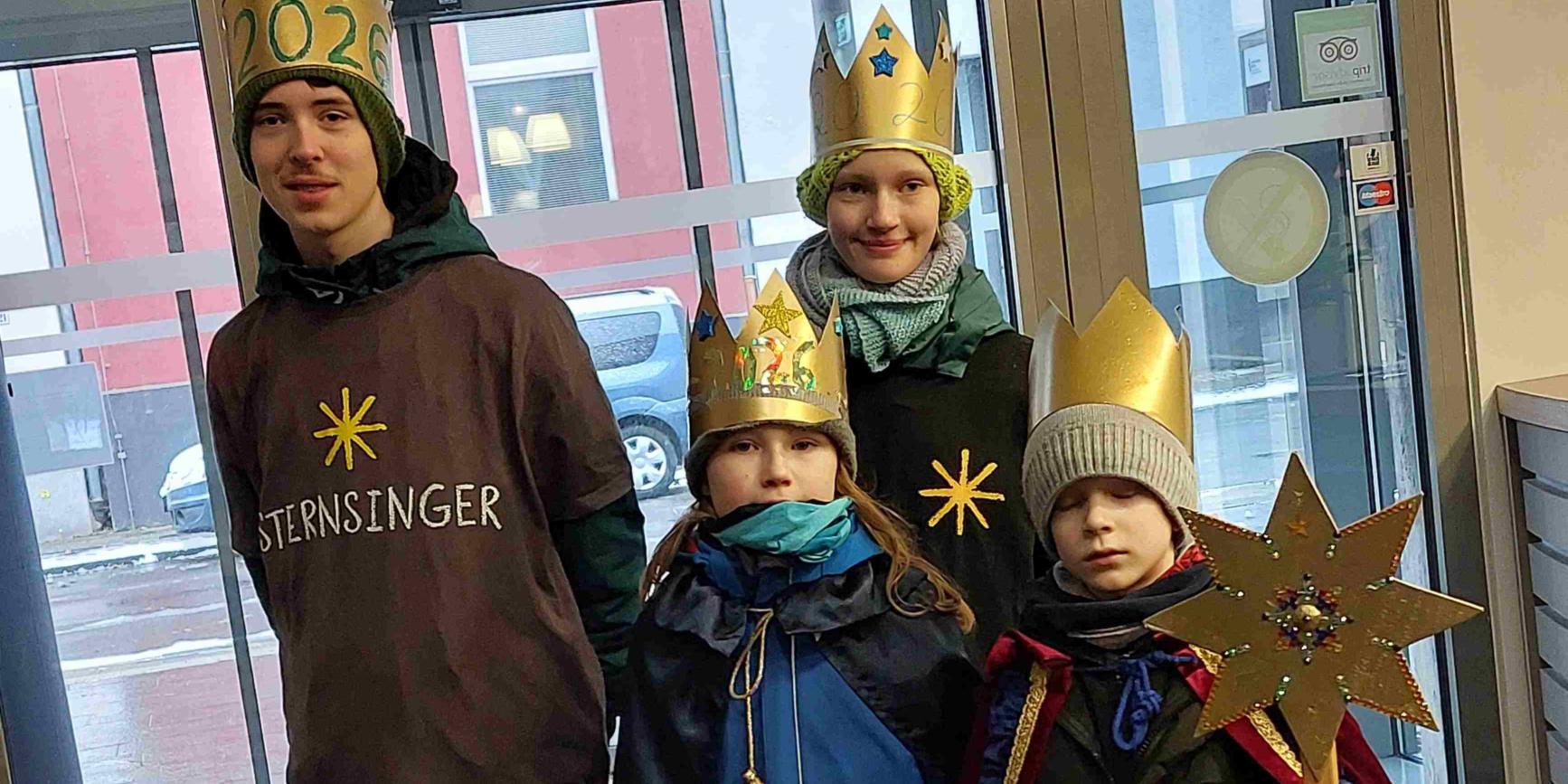 Vier Kinder, als Sternsinger mit Kronen und Stern, vor der Eingangstür der Akademie.