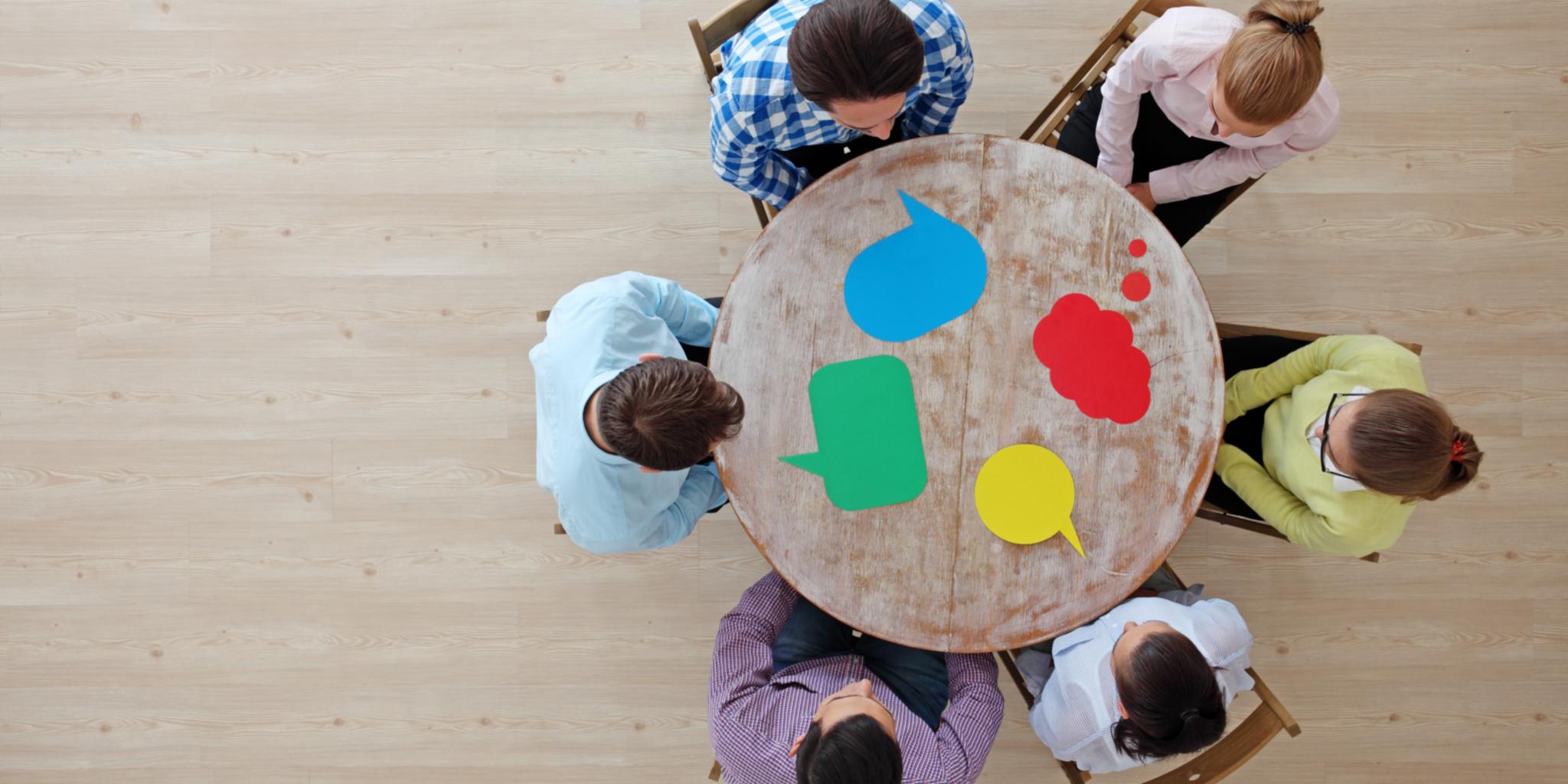 Menschen sitzen um einen Tisch, vor ihnen liegen Sprechblasen in unterschiedlicher Form.