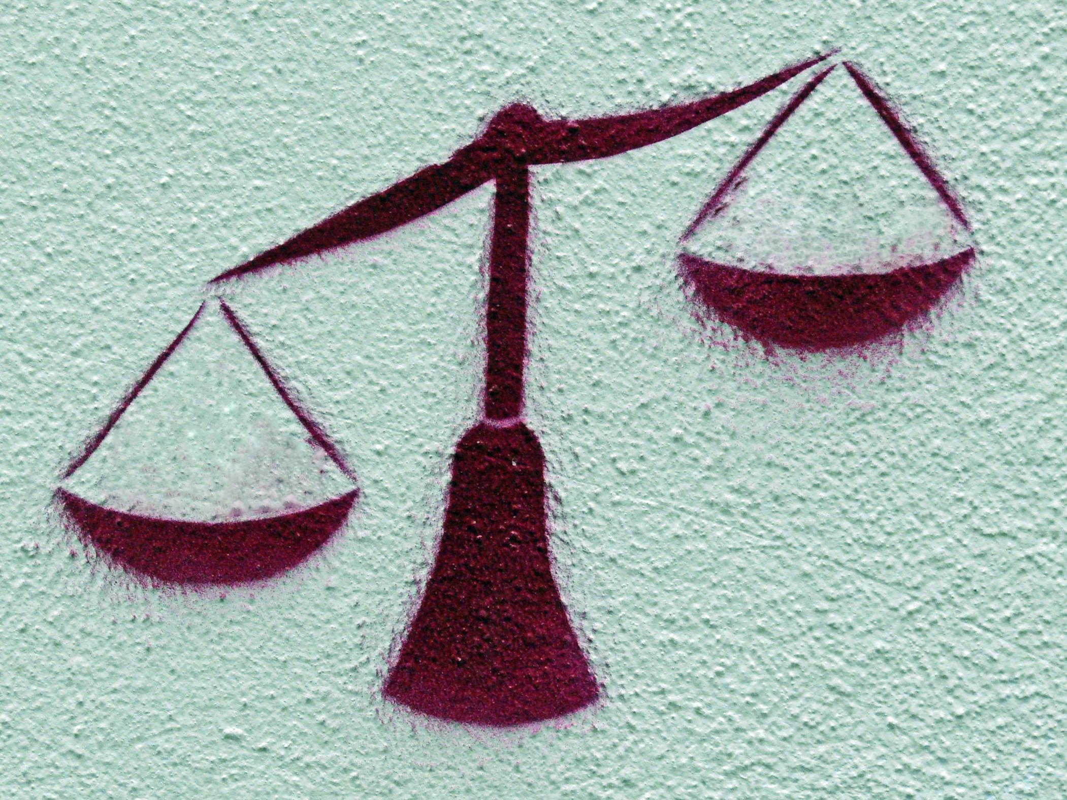 Graffito: An die Wand gesprayte Waage, die linke Waagschale ist tief, die rechte hoch.