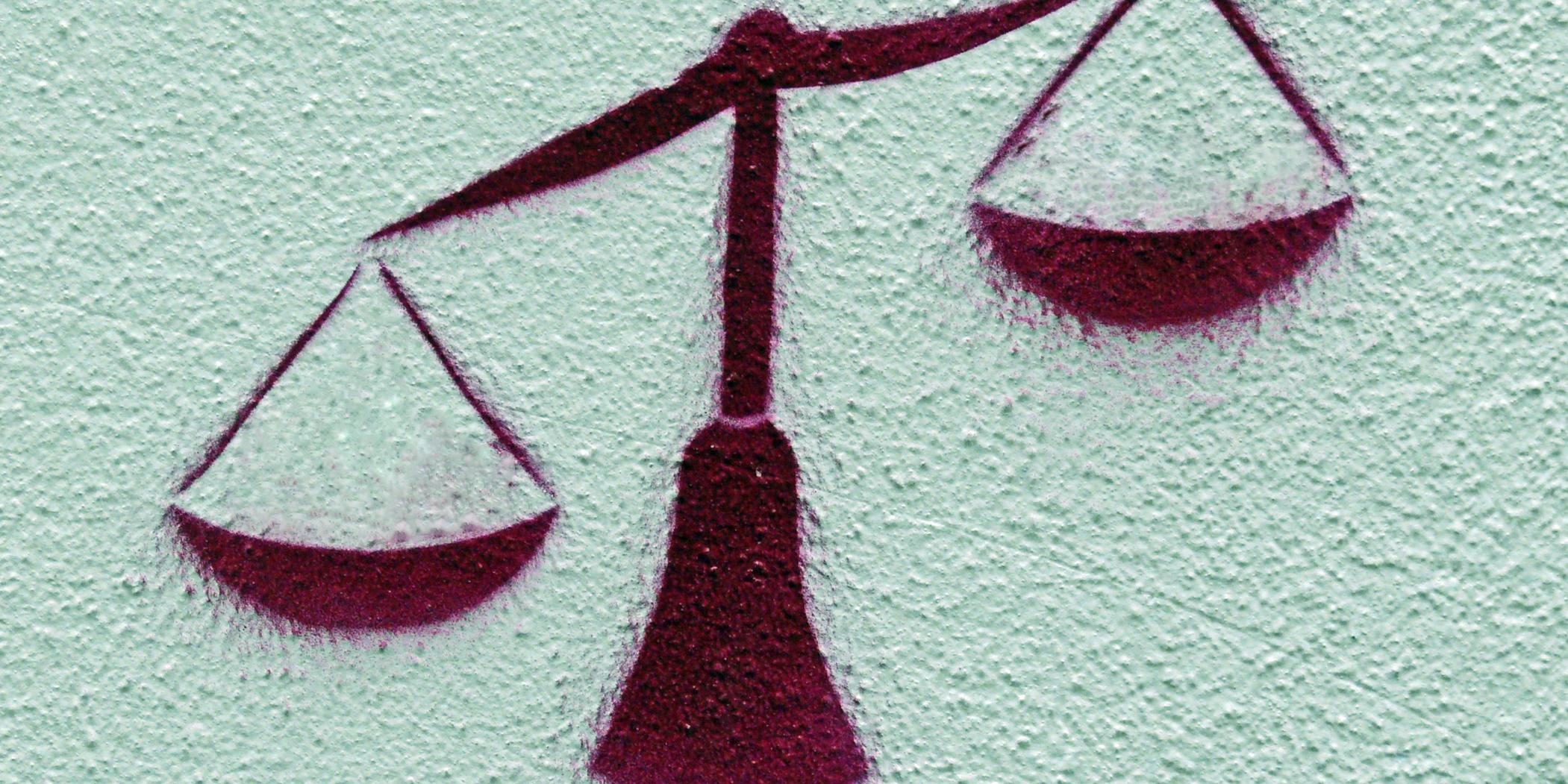 Graffito: An die Wand gesprayte Waage, die linke Waagschale ist tief, die rechte hoch.