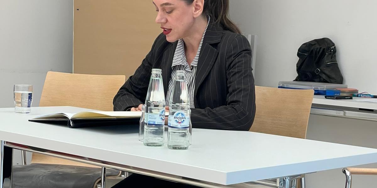 Eine Frau sitzt an einem Tisch mit einer aufgeschlagenen Textmappe und liest daraus. Es ist Luise Berndt, eine Schauspielerin vom Theater Aachen, am Tag des offenen Denkmals in der Akademie des Bistums Aachen. Vor ihr auf dem Tisch stehen Wasserflaschen.