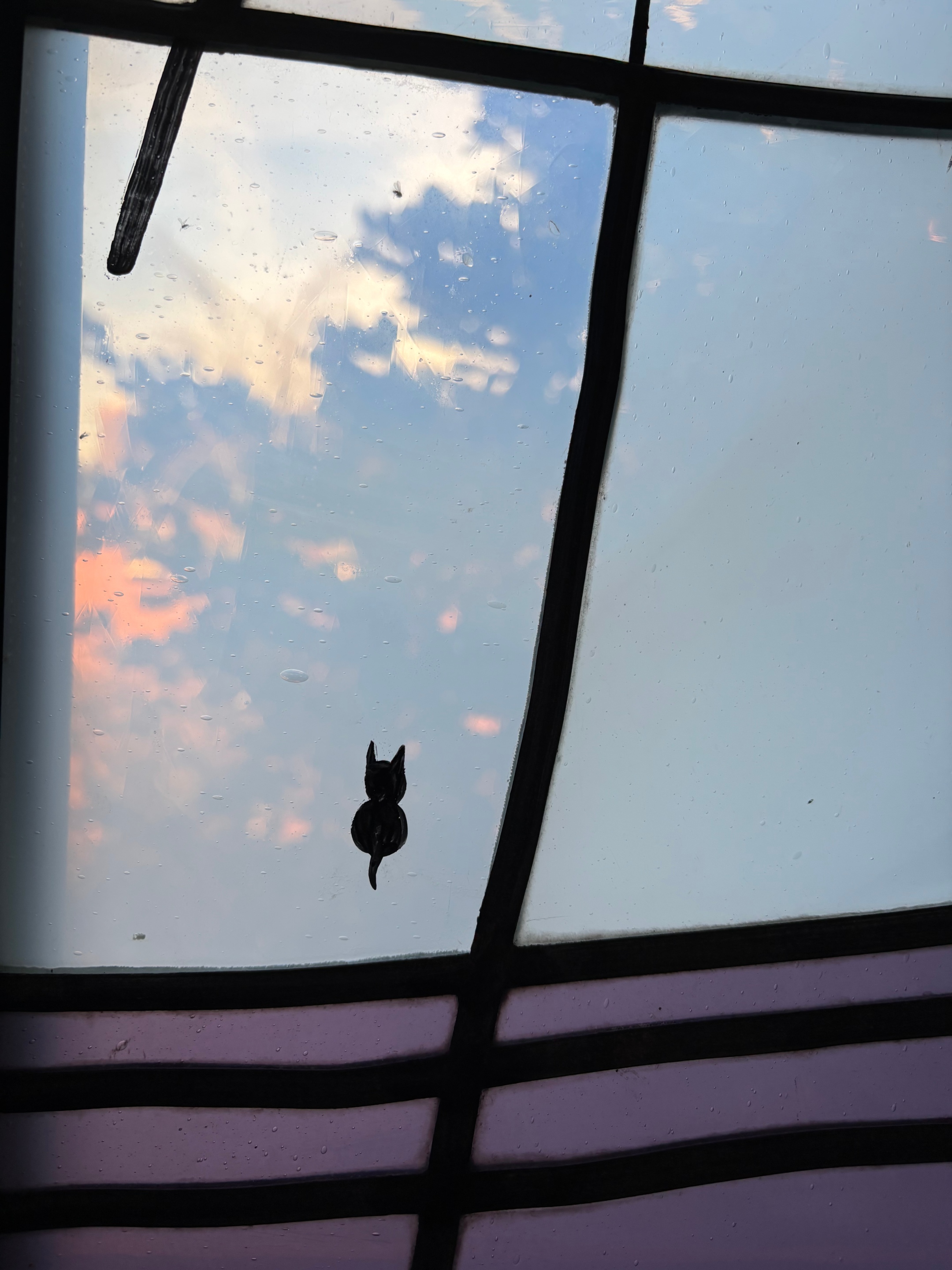 Eine Glasmalerei als Fenster in einem Kloster, eine kleine schwarze Katze mit dem Rücken zum Betrachter als Signatur der Künstlerin, Maria Katzgrau