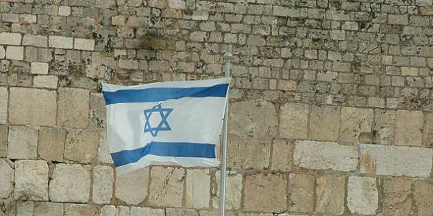 Israelische Flagge (zwei Streifen mit Davidsstern) vor einer Steinmauer.