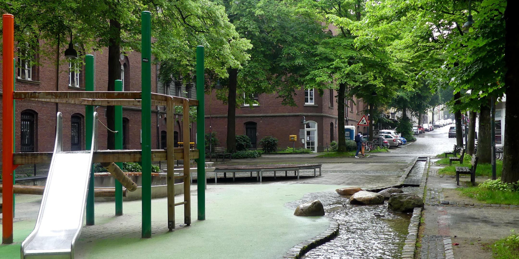 Ein Platz in der Innenstadt mit Kinderrutschbahn, ein schmaler Wasserlauf im Boden.