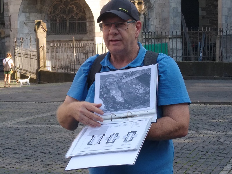 Ein Archäologe hält eine Mappe mit Einsteckhüllen in der Hand und zeigt ein Bild einer Ausgrabungssituation.