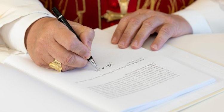 Hände des Papstes über dem Dokument der Enzyklika 'Magnifica humanitas', mit dem Füller in der rechten Hand setzt er die Unterschrift unter das Dokument.