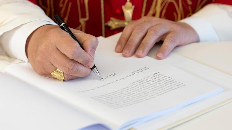 Hände des Papstes über dem Dokument der Enzyklika 'Magnifica humanitas', mit dem Füller in der rechten Hand setzt er die Unterschrift unter das Dokument.