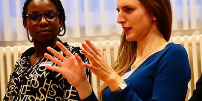 Zwei Frauen, offenbar Beteiligte in einer Gesprächsrunde, die eine beschreibt etwas mit ihren Händen.