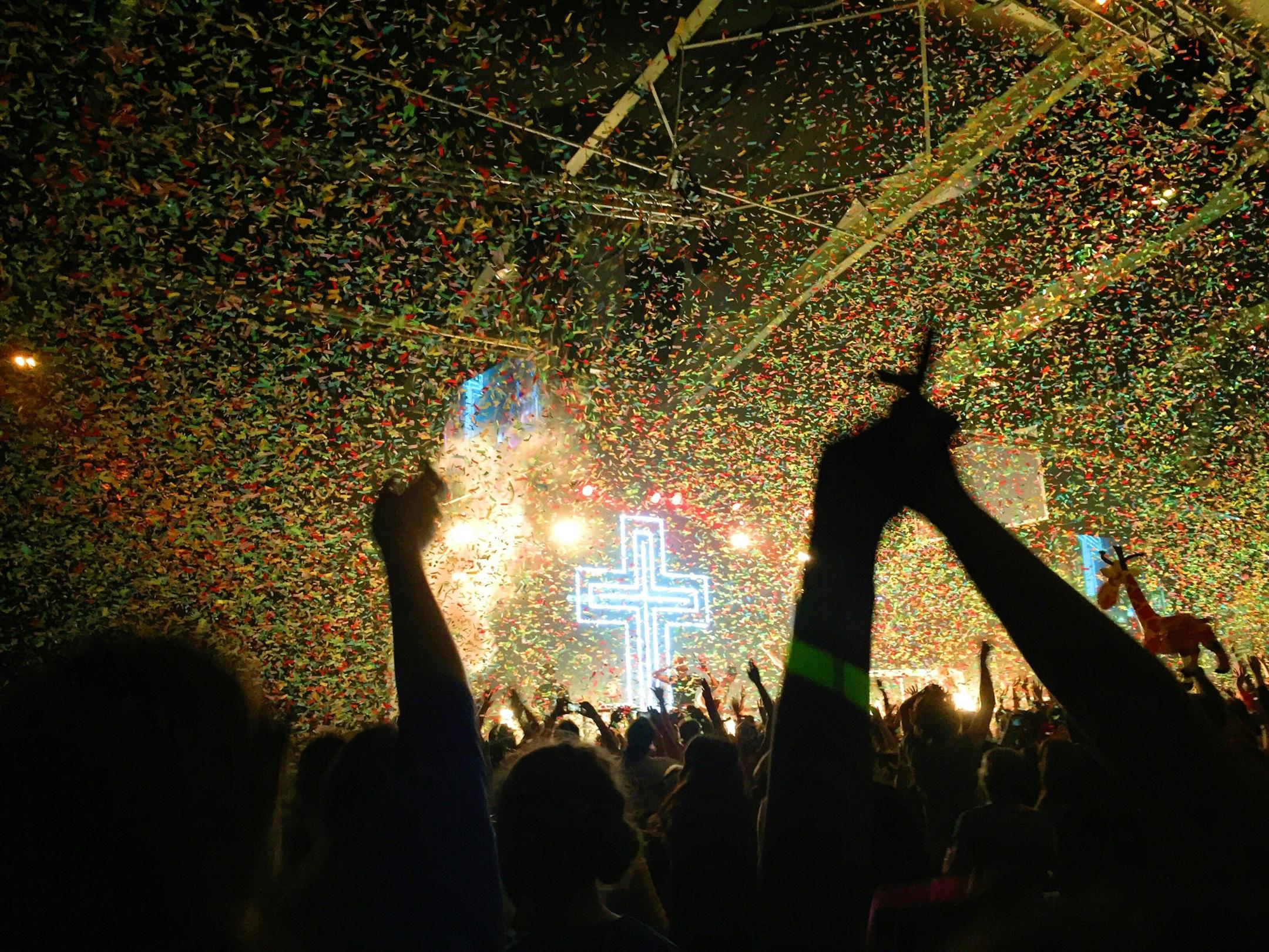 Ein erleuchtetes Kreuz, davor eine Menge von Menschen, einige mit erhobenen Armen.