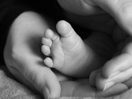 Erwachsenenhände umschließen einen Babyfuß.