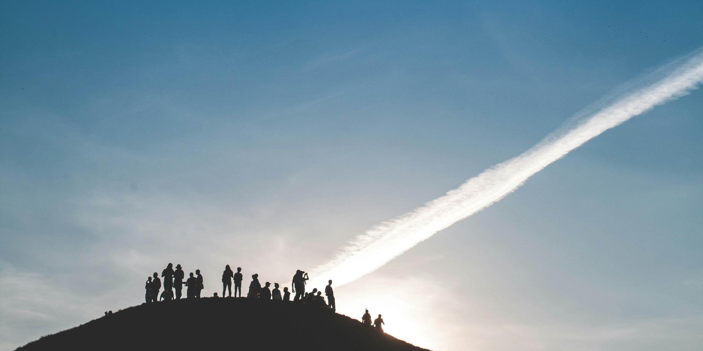 Eine Gruppe von Menschen steht auf einem Hügel und schaut in den Himmel.