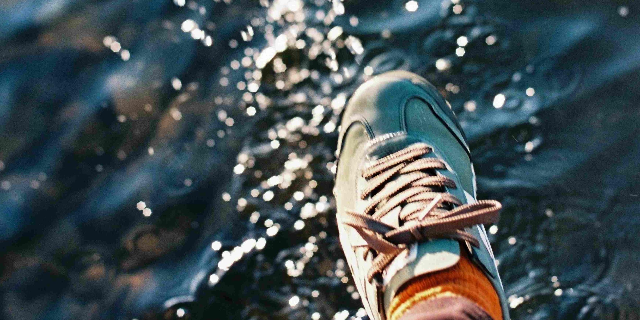 Ein Fuß mit einem Turnschuh schwebt über einer glitzernden Wasseroberfläche, als wolle er gleich darauftreten.