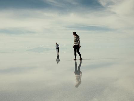Spiegelungen (c) Peter Conlan/unsplash Zwei Personen gehen wie auf Wolken, blicken sich an, sie spiegeln sich im Untergrund.