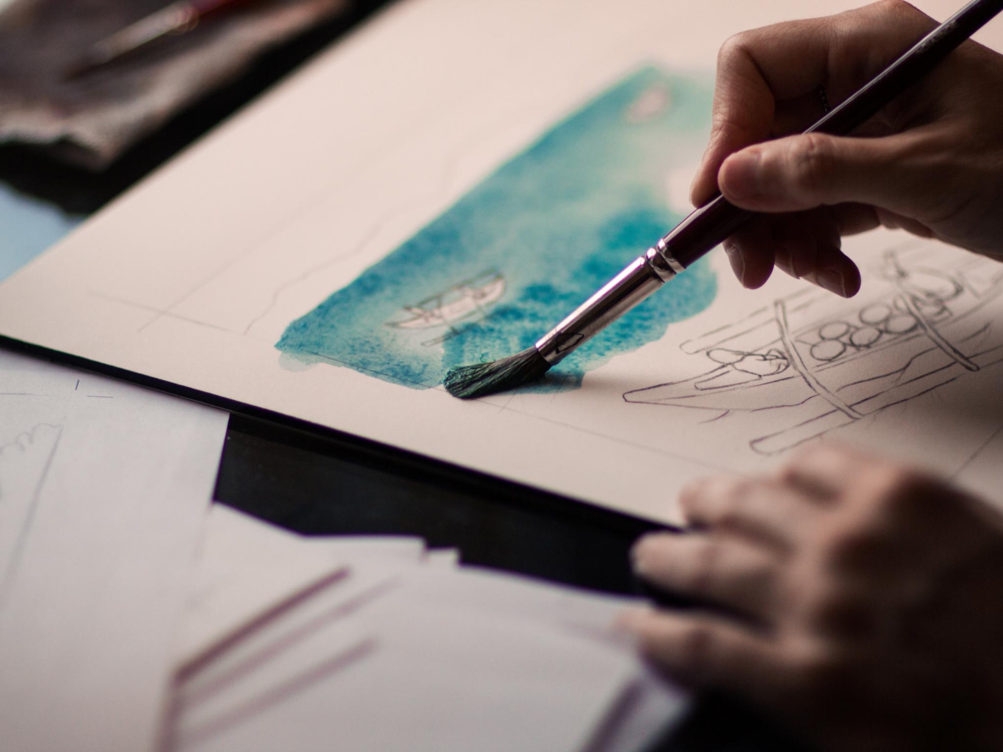 Hand einer Frau, die ein Aquarell malt.