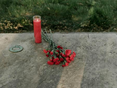 Grabstein mit Kerze und daraufgelegten Blumen.