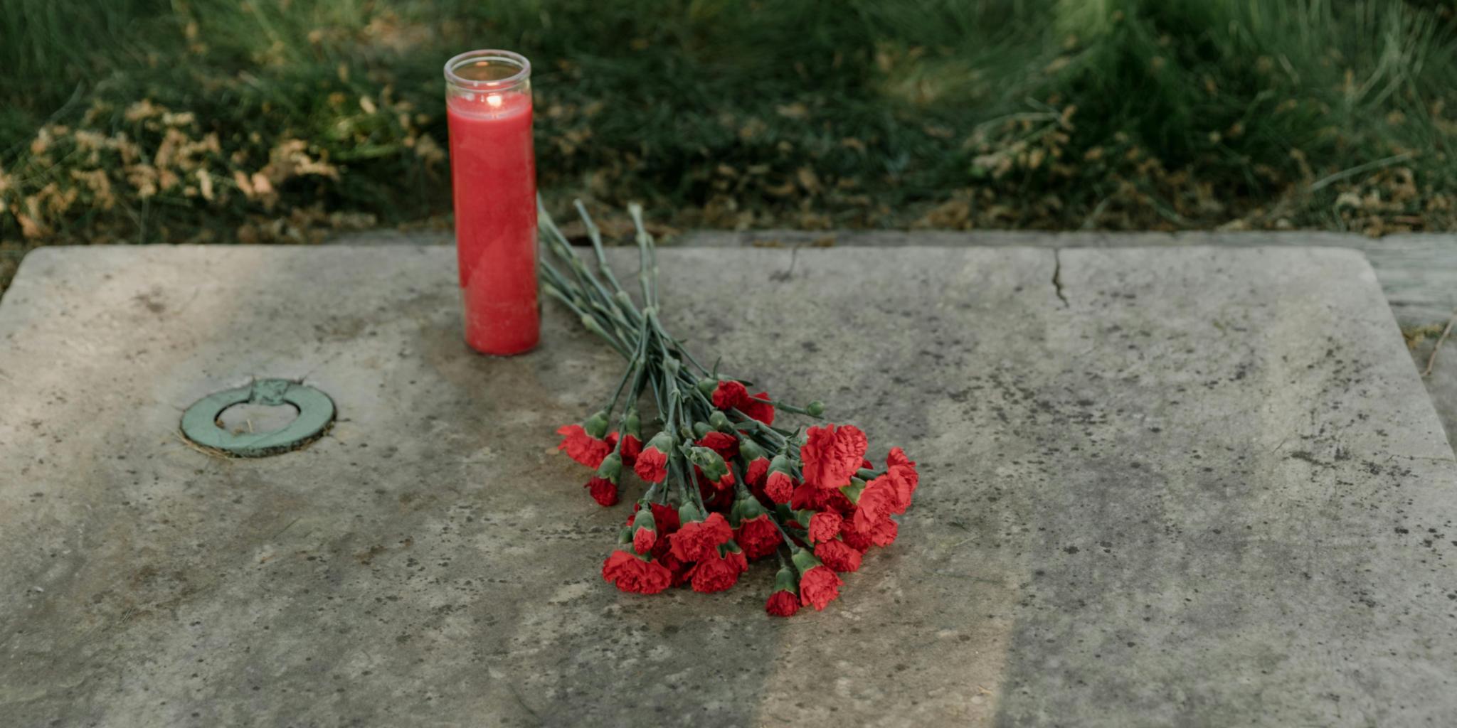 Grabstein mit Kerze und daraufgelegten Blumen.