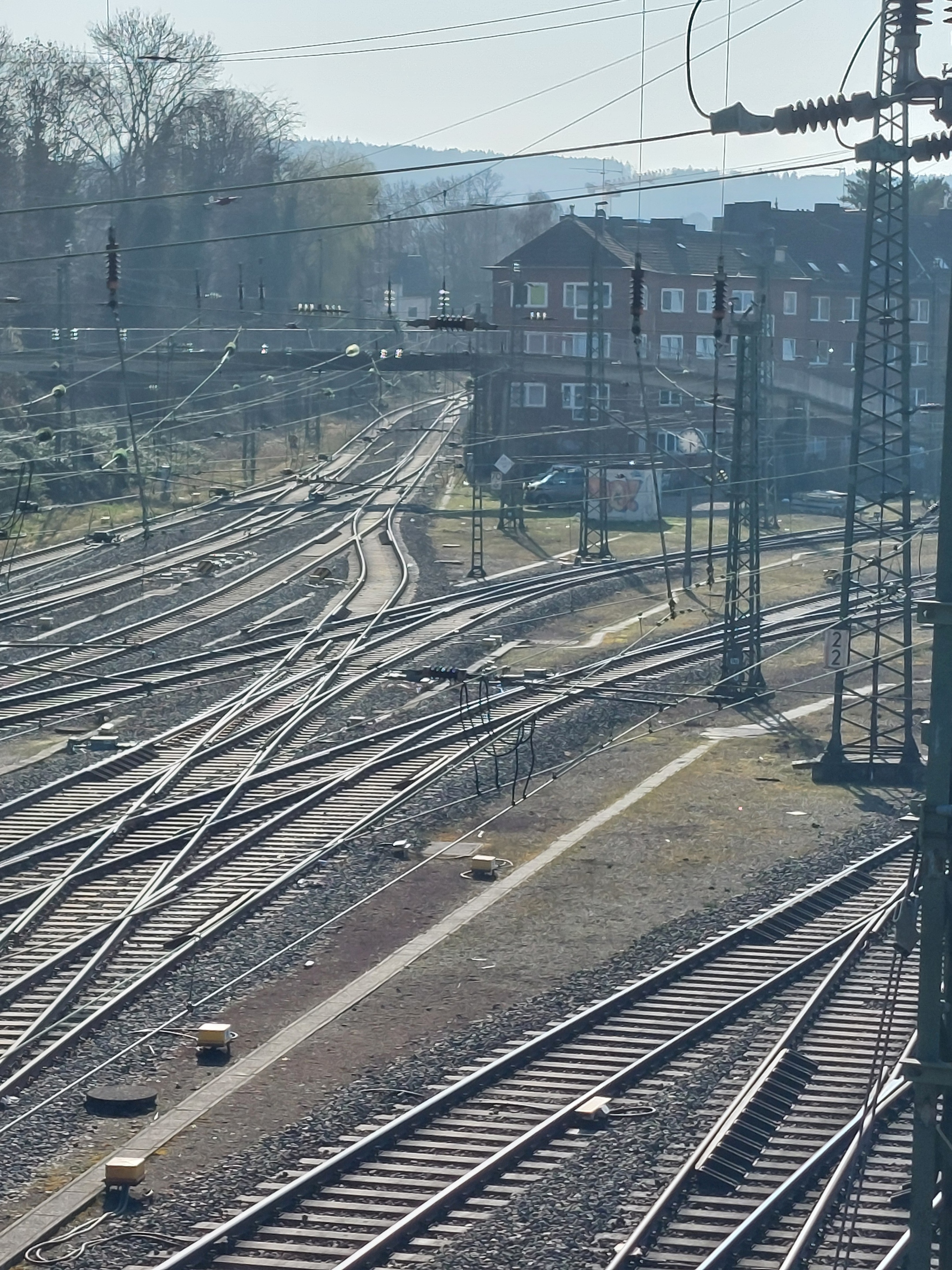Blick von einer Eisenbahnbrücke auf Bahngleise, im Hintergrund Häuser und bewaldete Hügel.